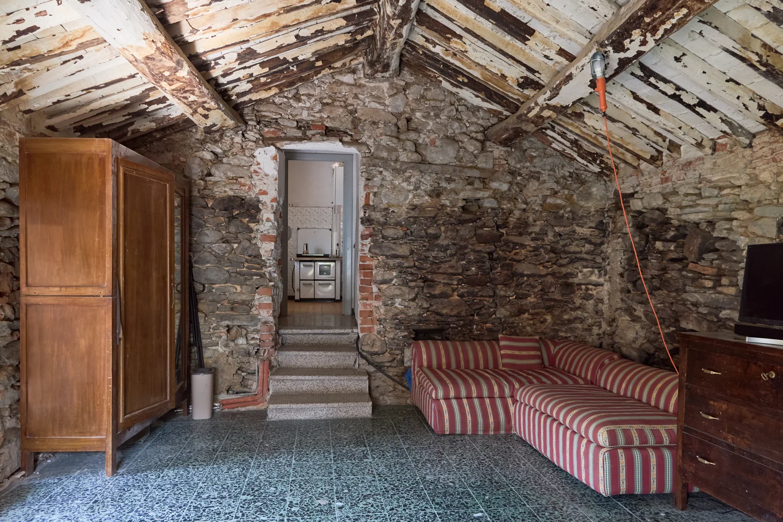 Room in Casa del Forno with stone walls, exposed beams, a sofa and a wooden wardrobe.