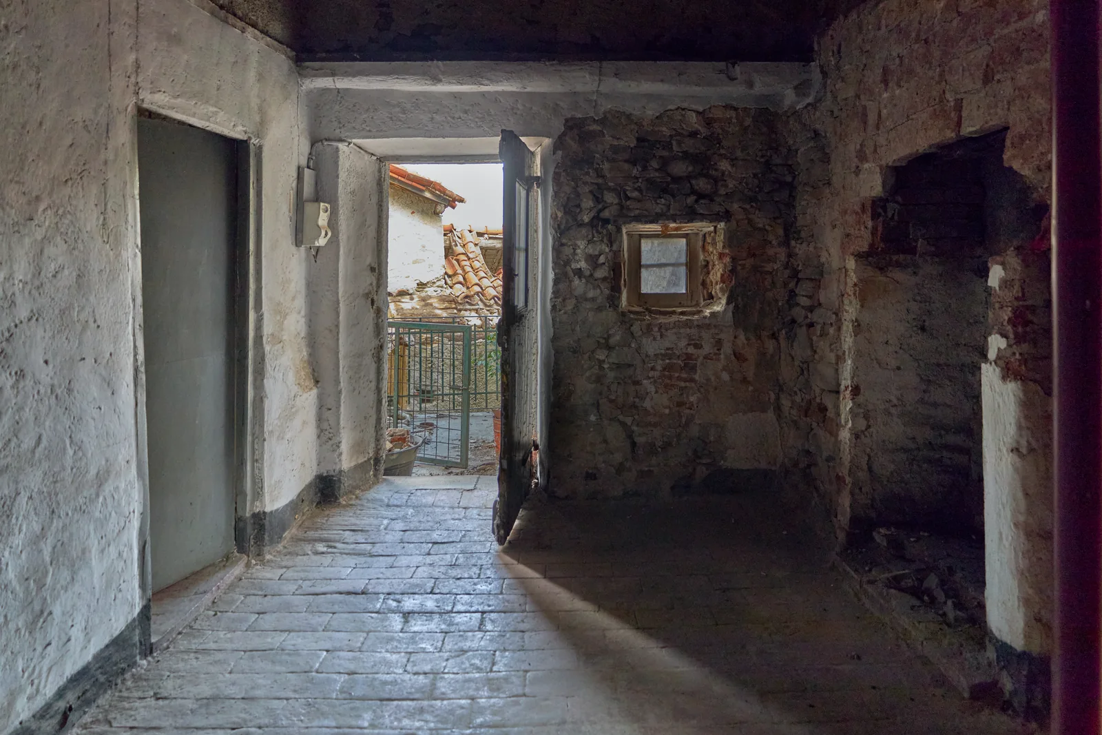 Unfinished interior in Casa del Noce, with an uneven floor and a doorway towards a balcony.