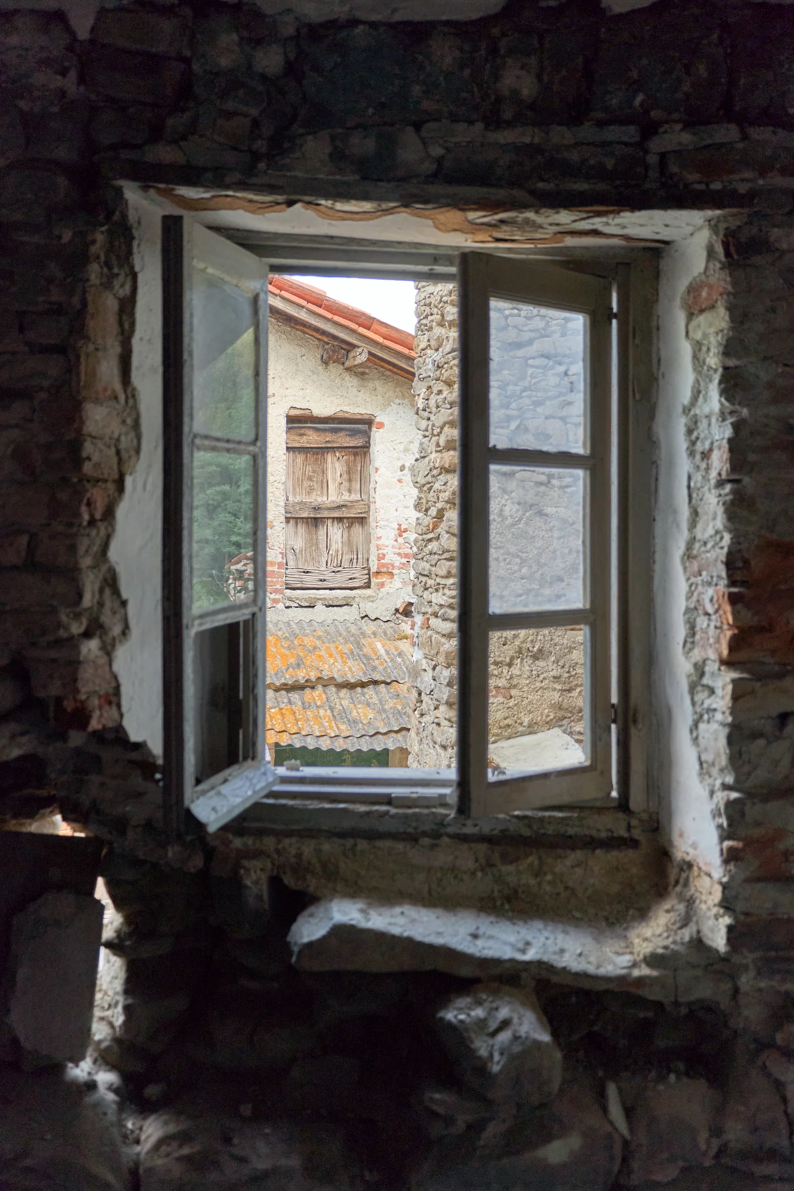 Open window in a stone wall in Casa del Noce, with rustic roofs outside.